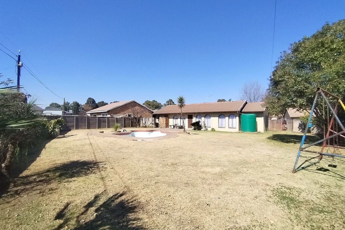 Rear view of the property featuring a swimming pool, large garden area, water tank, and a single-story house with arched windows.
