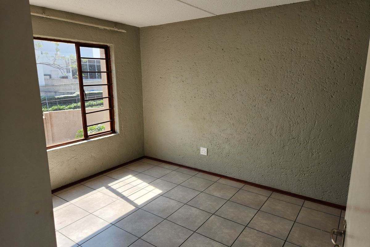An empty bedroom featuring neutral tiled flooring, textured walls, and a window with security bars, offering a blank canvas for personalization.