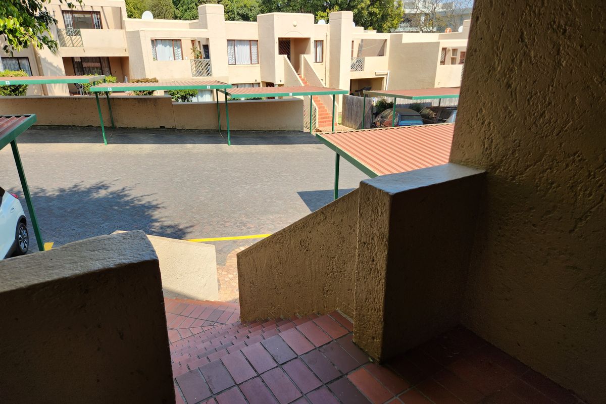 View of the apartment complex exterior, featuring a paved parking area with carports and a tiled staircase leading to the unit.