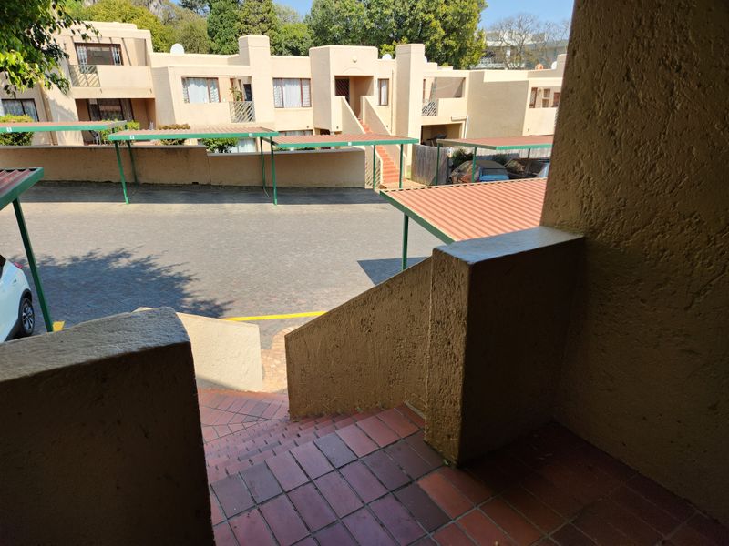 View of the apartment complex exterior, featuring a paved parking area with carports and a tiled staircase leading to the unit.