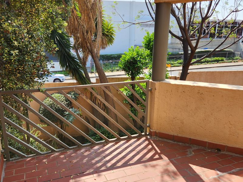 A private balcony featuring terracotta tiling, a metal balustrade, and a built-in braai area, overlooking the surrounding complex grounds.