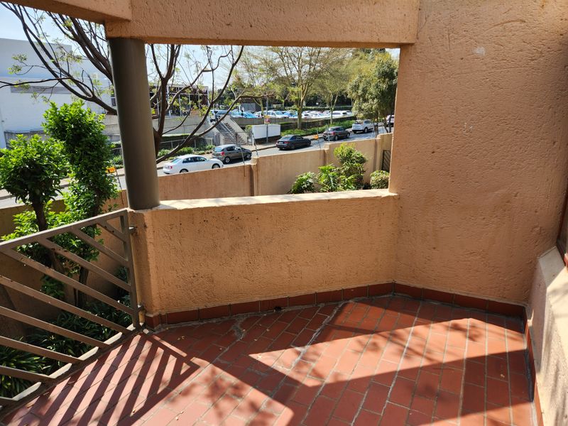 A covered balcony featuring terracotta tiled flooring, a metal balustrade, and a structural column, offering an elevated view of the street and surrounding area.