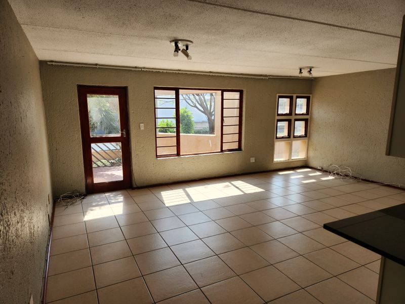 Spacious, empty living area featuring tiled flooring, textured walls, and natural light through timber-framed windows and a door leading to the exterior.