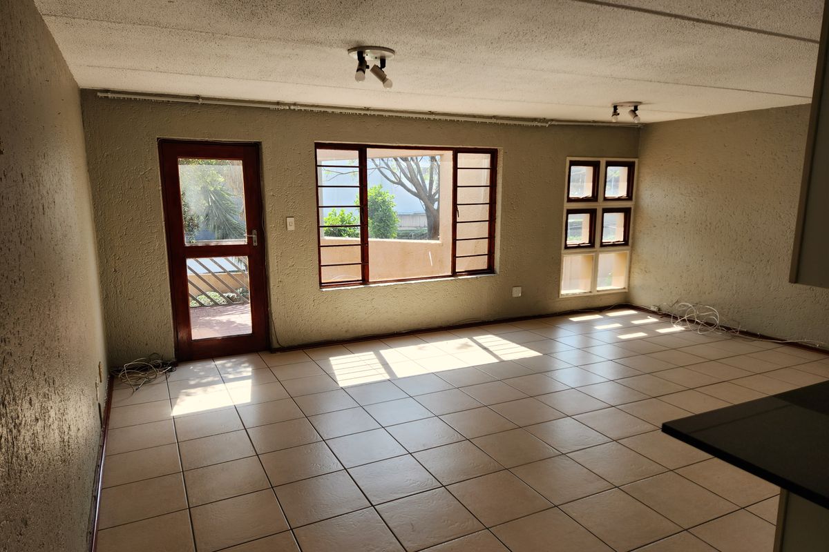 Spacious, empty living area featuring tiled flooring, textured walls, and natural light through timber-framed windows and a door leading to the exterior.