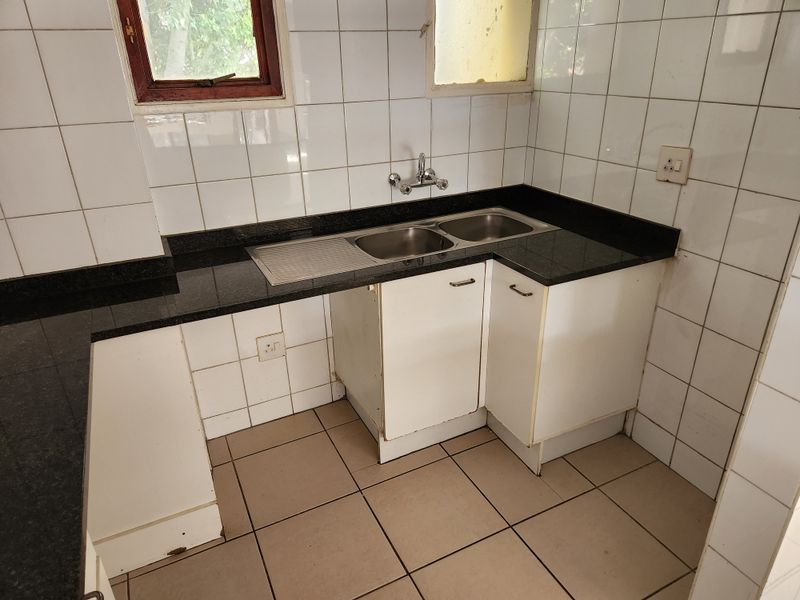 A compact kitchen area featuring granite countertops, a double stainless steel sink, and tiled splashbacks, currently vacant and ready for updates.