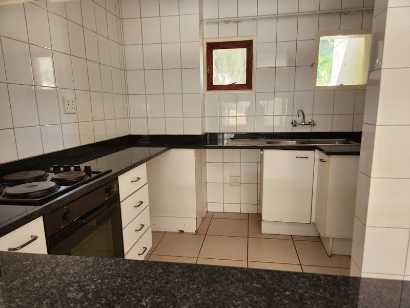 A functional kitchen featuring granite countertops, built-in oven and hob, double sink, and tiled finishes throughout, offering a blank canvas for modern updates.