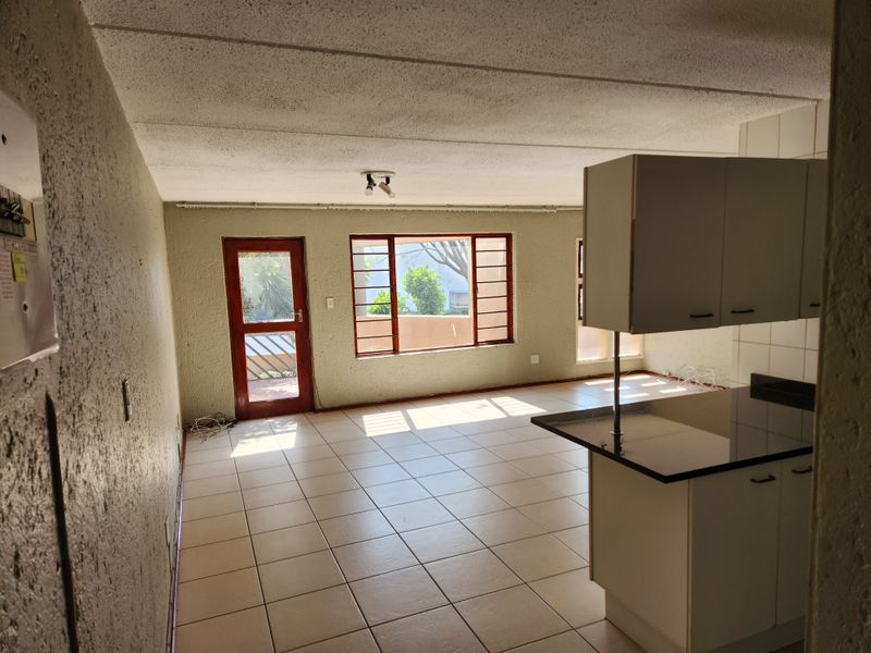 An open-plan living and kitchen area featuring ceramic floor tiles, textured walls, and basic cabinetry, offering a blank canvas for renovation.
