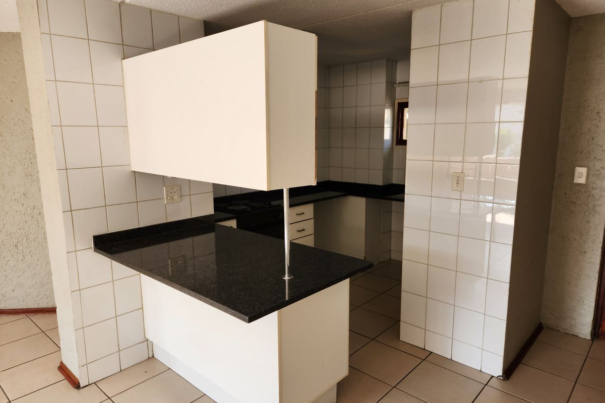 An empty, dated kitchen featuring tiled walls, granite countertops, and a breakfast bar, offering a blank canvas for modern renovation.