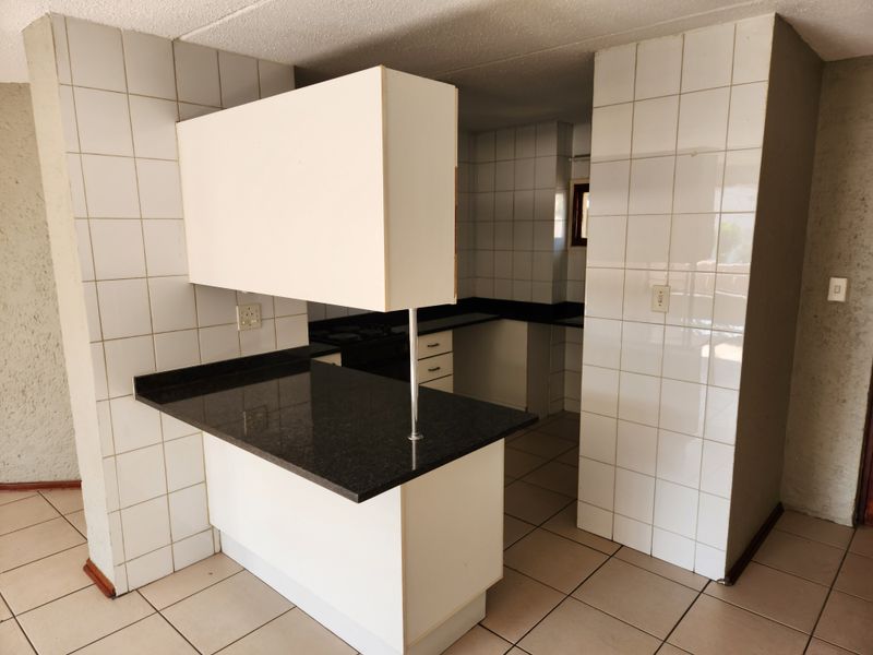 An empty, dated kitchen featuring tiled walls, granite countertops, and a breakfast bar, offering a blank canvas for modern renovation.