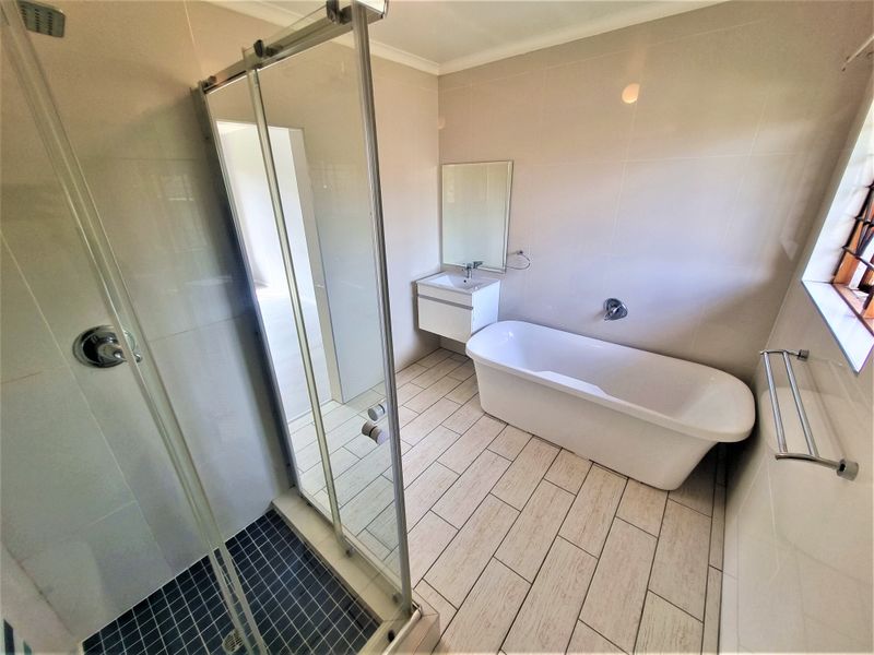 Modern bathroom featuring a freestanding bathtub, a separate glass-enclosed shower, and a wall-mounted vanity with neutral tiling throughout.