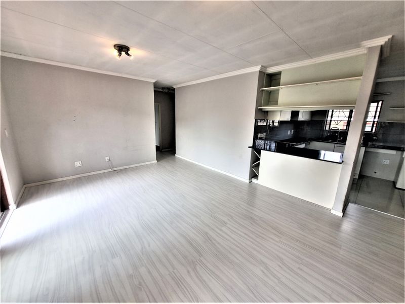 An open-plan living and kitchen area featuring light-toned laminate flooring, neutral walls, and a functional kitchen with granite countertops and built-in cabinetry.