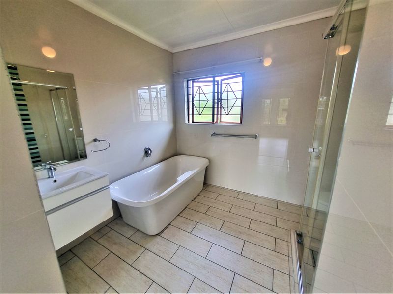Modern bathroom featuring a freestanding bathtub, glass shower enclosure, and a wall-mounted vanity with neutral wall and floor tiling.