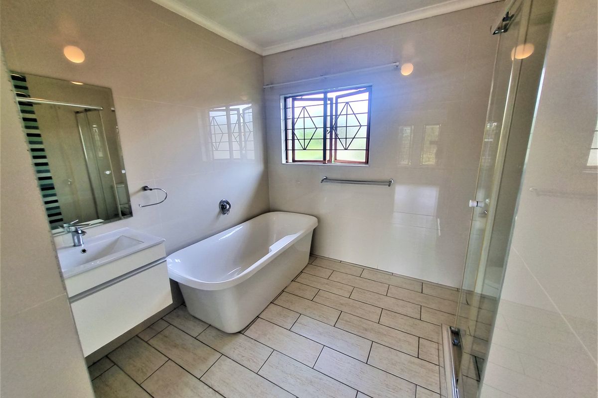 Modern bathroom featuring a freestanding bathtub, glass shower enclosure, and a wall-mounted vanity with neutral wall and floor tiling.
