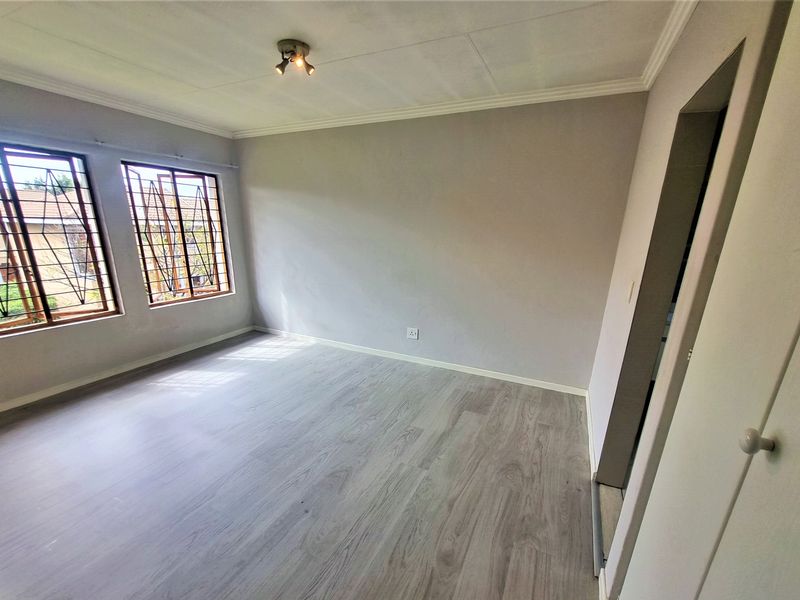 A bright, empty bedroom featuring modern laminate flooring, neutral walls, and security bars on the windows.