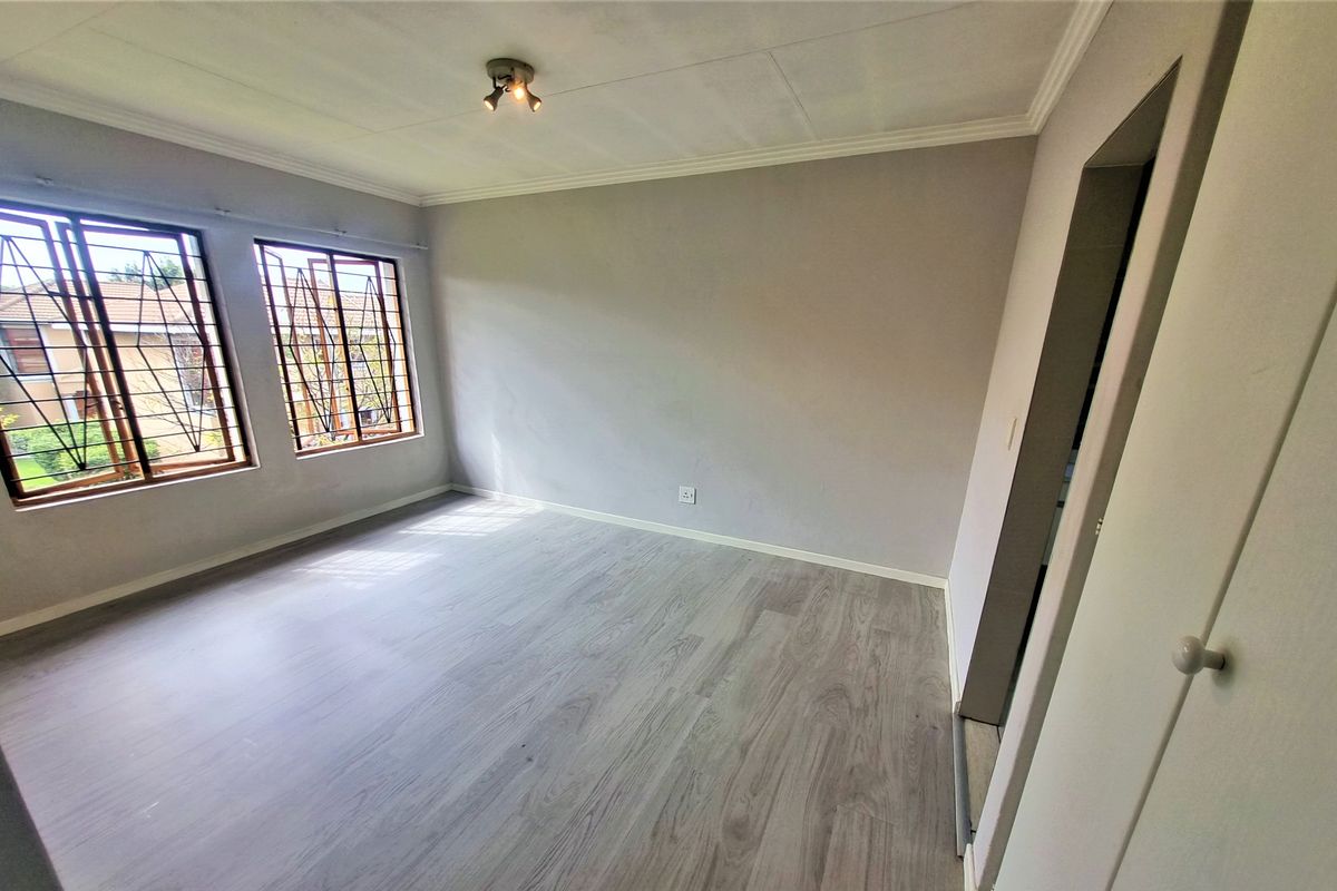 A bright, empty bedroom featuring modern laminate flooring, neutral walls, and security bars on the windows.