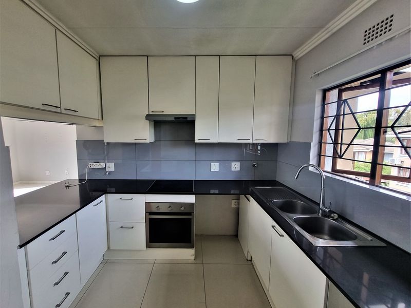A clean, functional kitchen featuring white cabinetry, black granite countertops, built-in oven and hob, and a double stainless steel sink.