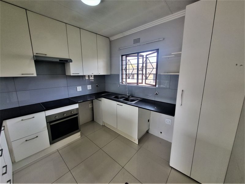 A clean, functional kitchen featuring white cabinetry, black countertops, built-in oven and hob, and tiled flooring. The space is vacant and ready for use.