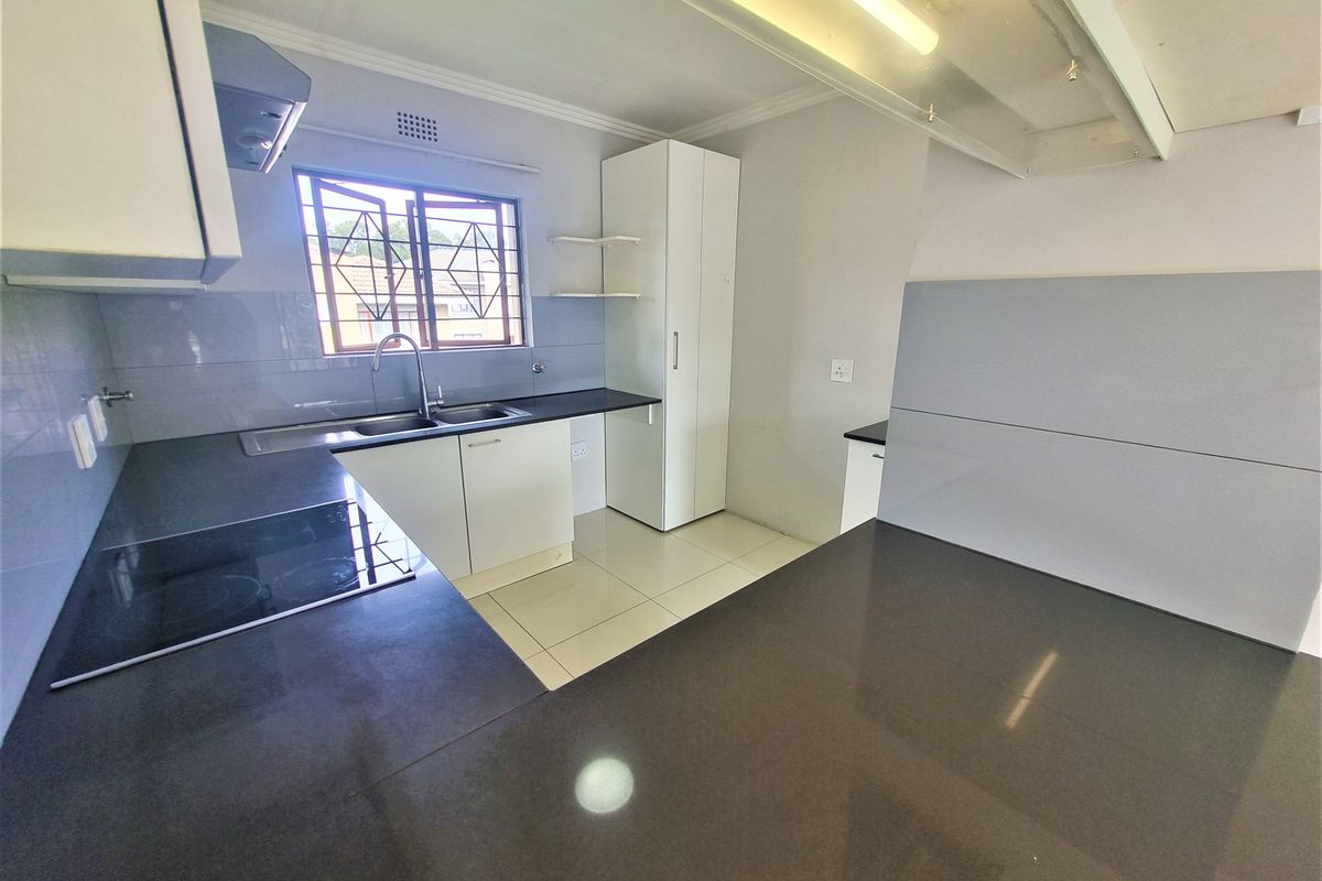 A clean, modern kitchen featuring white cabinetry, dark stone countertops, an integrated electric hob, and tiled flooring.