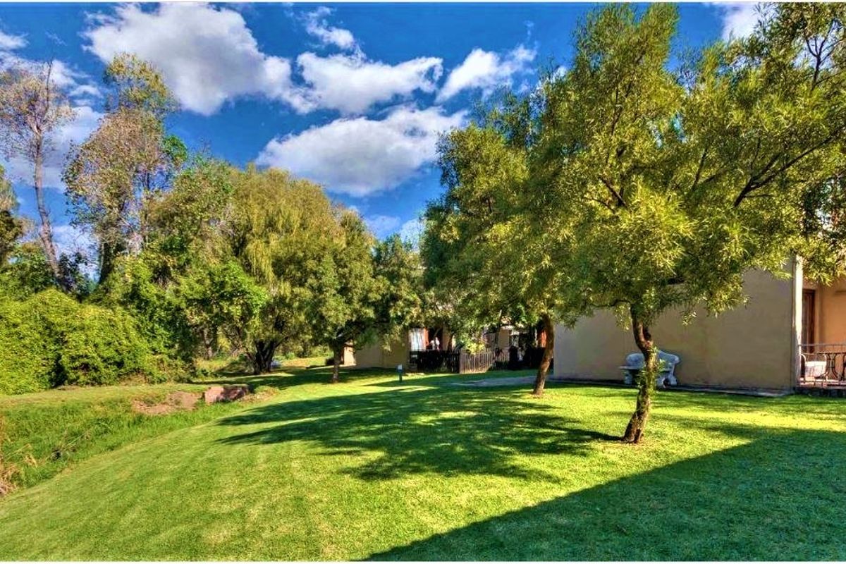 A view of the rear exterior of the townhouse, featuring a well-maintained lawn, mature trees, and a private patio area.