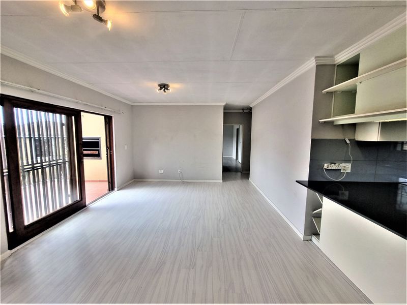 Spacious open-plan living area featuring light laminate flooring, modern kitchen cabinetry with granite countertops, and large sliding doors leading to an outdoor patio.