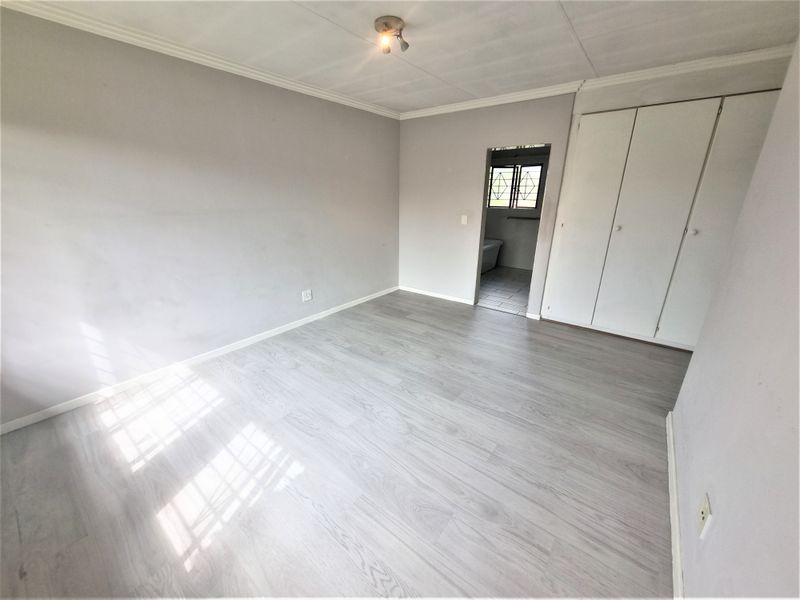 A bright, empty bedroom featuring light-toned laminate flooring, built-in cupboards, and direct access to an adjoining bathroom.