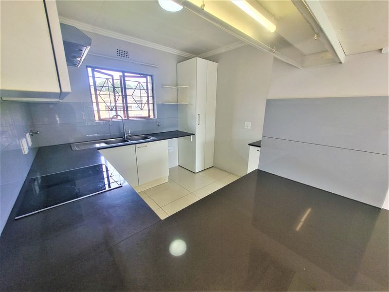 A clean, modern kitchen featuring white cabinetry, dark stone countertops, an integrated electric hob, and tiled flooring.
