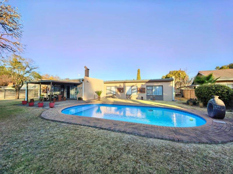 Rear exterior view featuring a swimming pool with brick coping, a covered patio area, and a chimney stack against the house facade.