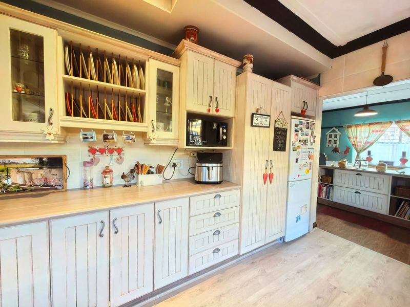 A country-style kitchen featuring cream-toned cabinetry, integrated storage solutions, plate racks, and durable laminate countertops with wood-look flooring.