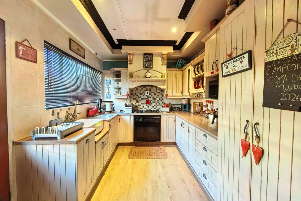 A country-style kitchen featuring built-in cabinetry, a tiled backsplash, integrated oven and hob, and wood-look laminate flooring.