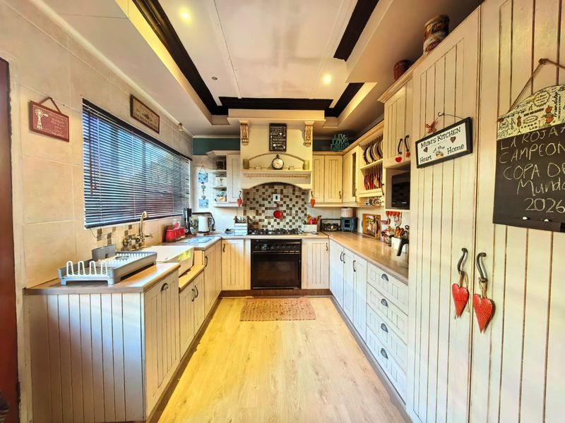 A country-style kitchen featuring built-in cabinetry, a tiled backsplash, integrated oven and hob, and wood-look laminate flooring.