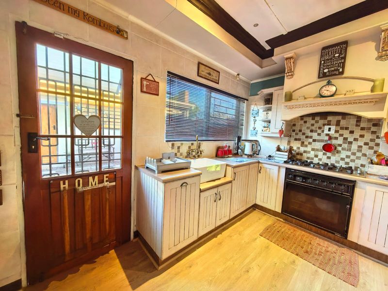 A rustic-style kitchen featuring white timber cabinetry, a farmhouse sink, built-in oven with gas hob, and a tiled backsplash with direct exterior access.