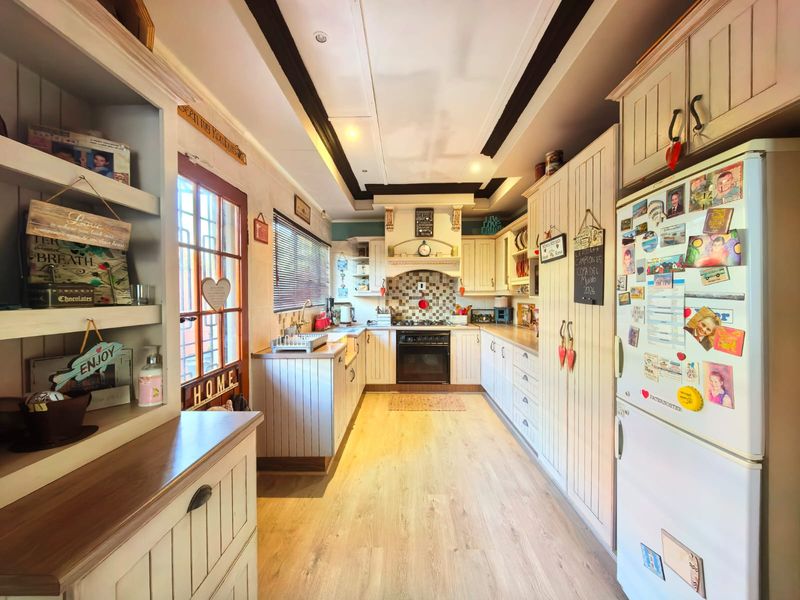 A galley-style kitchen featuring light-toned cabinetry, a gas stove with a decorative extractor hood, tiled backsplash, and wood-look laminate flooring.