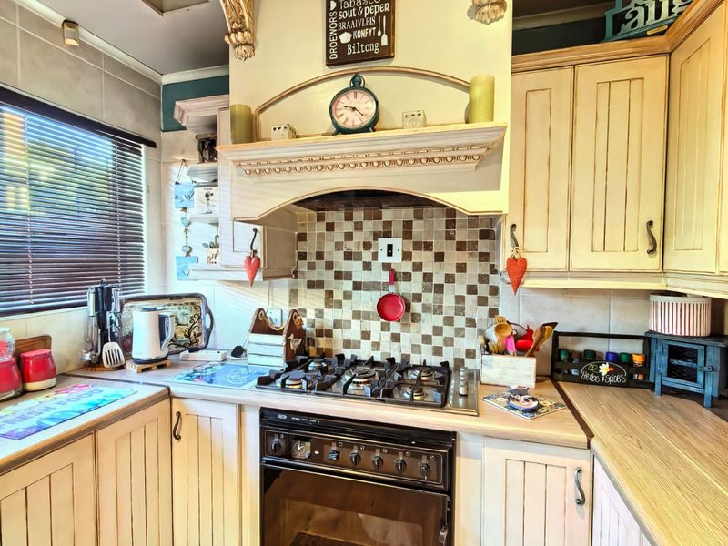A compact kitchen featuring timber cabinetry, a gas hob with integrated extractor hood, tiled backsplash, and laminate countertops.