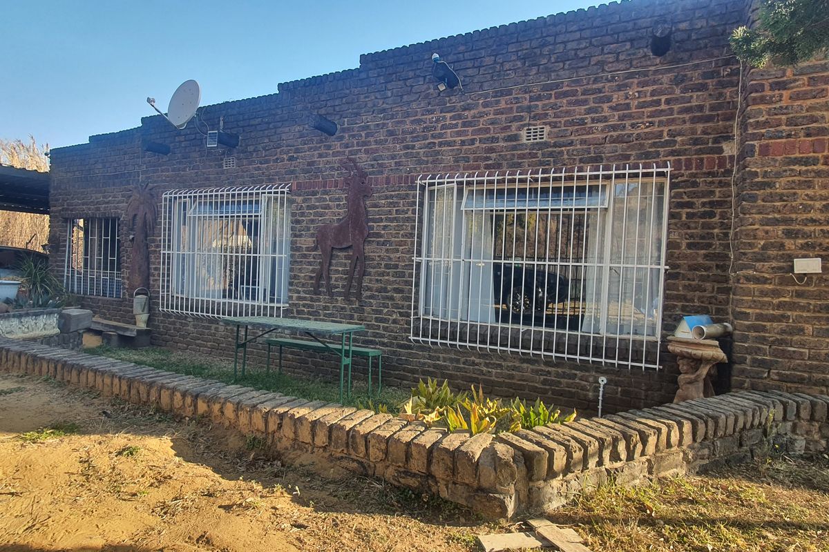 Rear exterior view of a face brick house featuring security bars on windows, a brick retaining wall, and an attached carport structure.