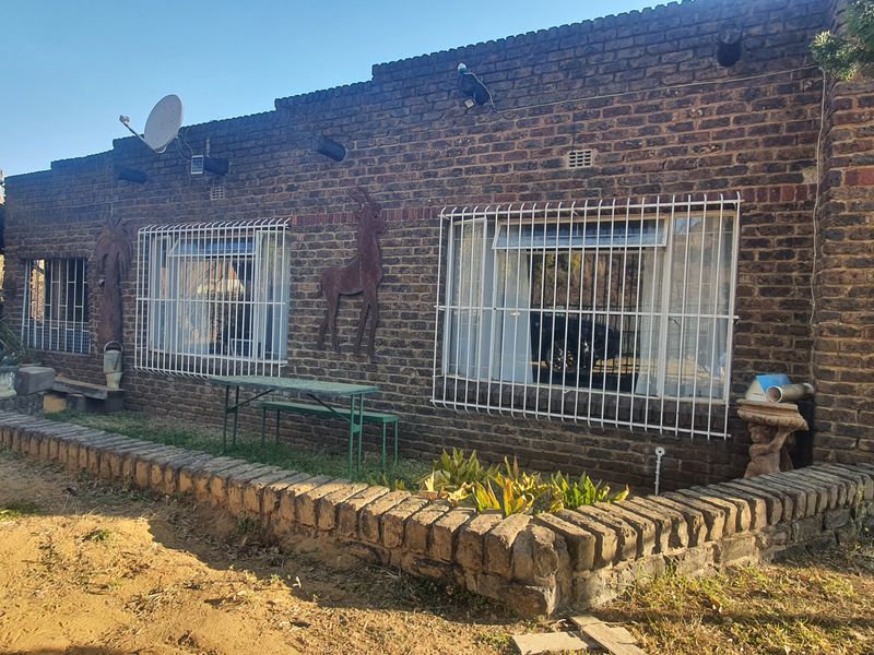 Rear exterior view of a face brick house featuring security bars on windows, a brick retaining wall, and an attached carport structure.