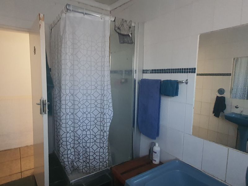 A functional bathroom featuring a shower enclosure, pedestal basin, and wall-mounted mirror, finished with tiled walls and flooring.