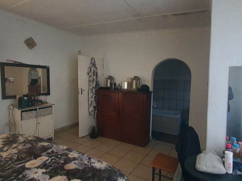 A bedroom featuring tiled flooring and an arched doorway leading to an en-suite bathroom, requiring cosmetic updates to improve the overall finish.