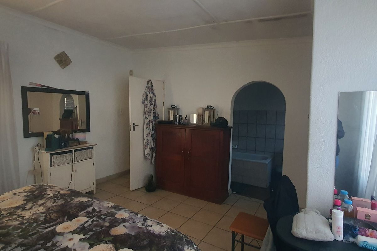 A bedroom featuring tiled flooring and an arched doorway leading to an en-suite bathroom, requiring cosmetic updates to improve the overall finish.