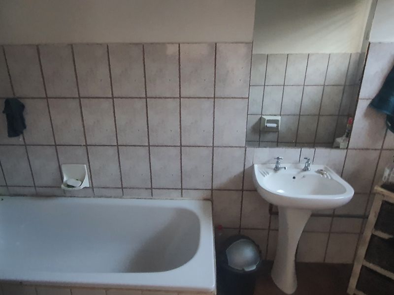 A dated bathroom featuring a pedestal basin, built-in bathtub, and wall-mounted mirror with tiled walls.