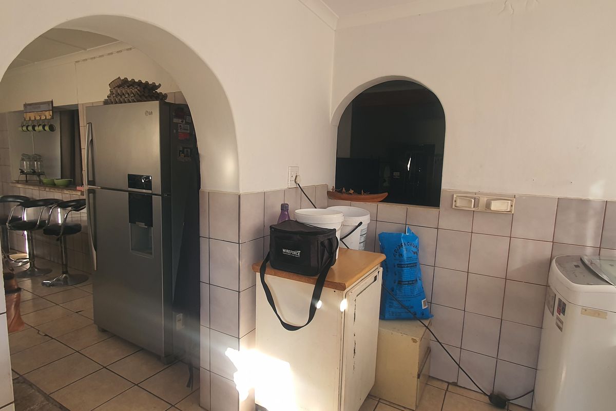 A functional kitchen area featuring tiled flooring, a tiled splashback, and an arched opening leading to an adjacent living space.