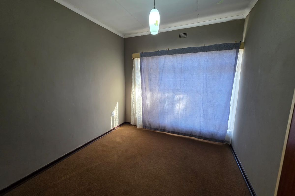 An empty bedroom featuring carpeted flooring, neutral wall finishes, and a central pendant light fixture, ready for renovation or staging.