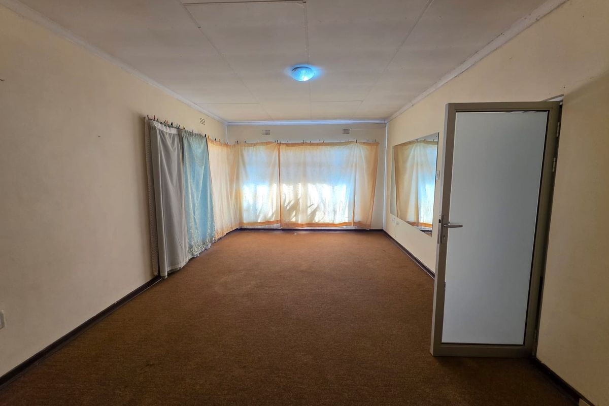 An empty living room featuring carpet flooring, a tiled ceiling, and a frosted glass door, offering a blank canvas for renovation.