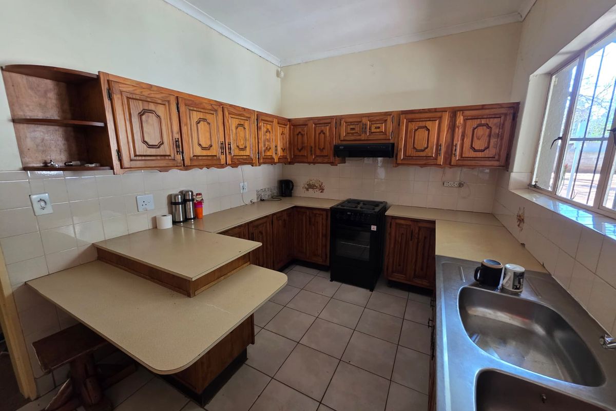 A functional kitchen featuring traditional wooden cabinetry, laminate countertops, a double stainless steel sink, and a freestanding stove with an extractor fan.