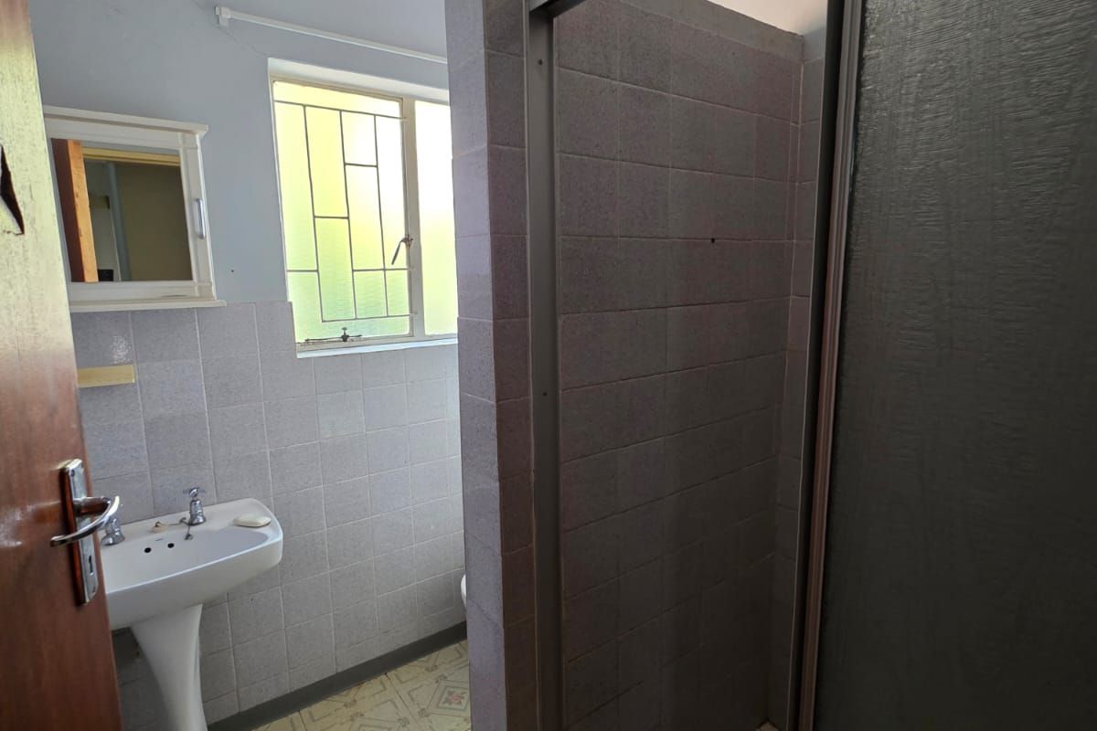 A functional bathroom featuring a pedestal washbasin, a tiled shower enclosure, and original floor tiling, offering potential for modernization.
