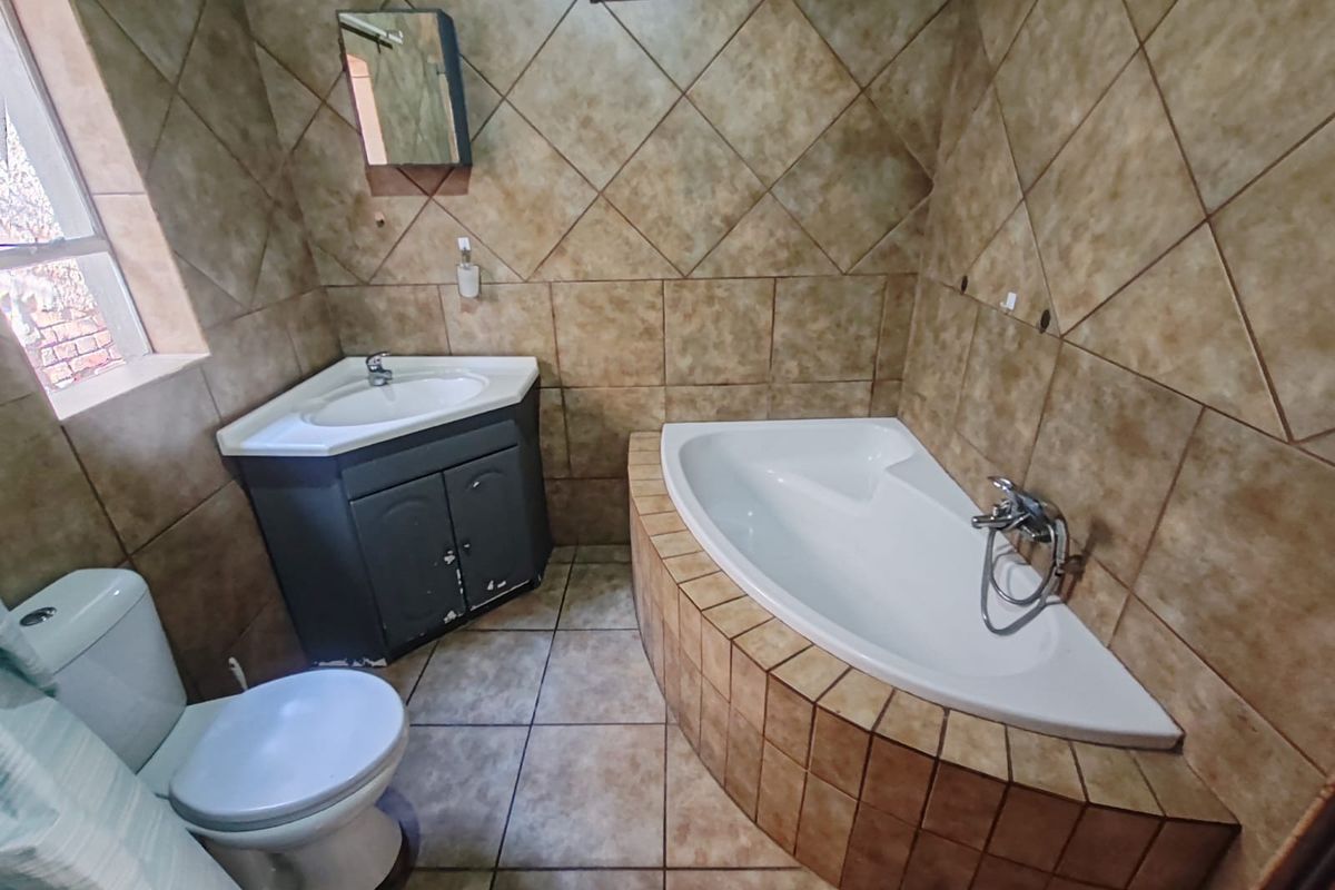 A functional bathroom featuring a corner bathtub, vanity cabinet with basin, and toilet, finished with full-height wall tiling and floor tiles.