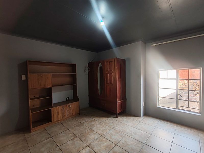 A bedroom featuring tiled flooring and a steel-framed window, requiring cosmetic updates to improve the overall aesthetic and finish.