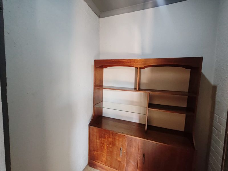 A small, enclosed corner space featuring plain walls and a built-in wooden storage unit.