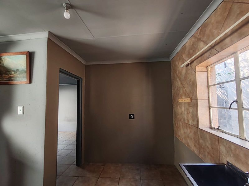 A functional kitchen area featuring tiled splashbacks, a steel window frame, and a sink, currently presented as an empty space ready for renovation.