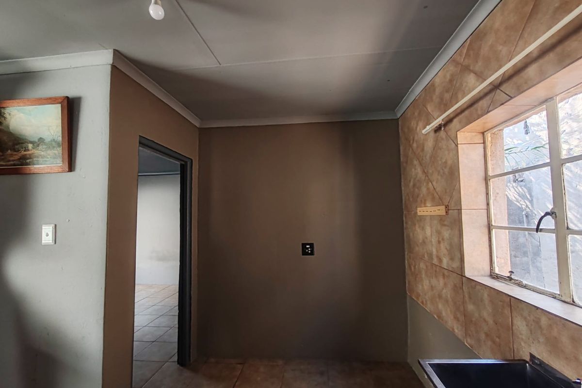 A functional kitchen area featuring tiled splashbacks, a steel window frame, and a sink, currently presented as an empty space ready for renovation.