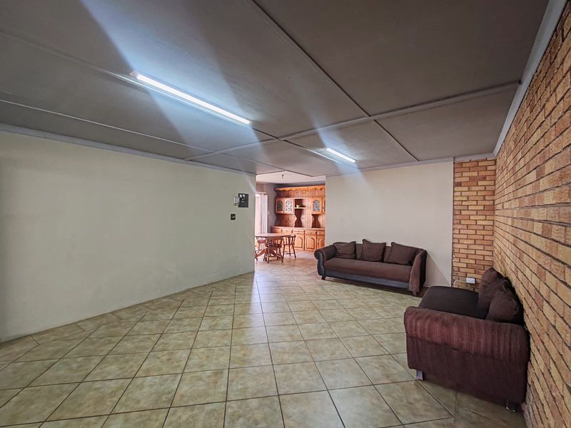Open plan living area featuring ceramic floor tiles, exposed brick feature wall, and fluorescent lighting, offering a spacious layout for renovation.